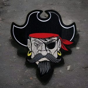 May include: Embroidered patch of a cartoon pirate with a black hat, red bandana, and an eye patch. The pirate has a gray beard and mustache, and gold earrings.
