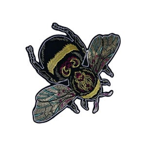 May include: An embroidered patch shaped like a bumblebee with a black body, yellow fuzzy accents, and intricate wings featuring metallic gold, teal, and magenta thread details. The insect design has a black border and detailed stitching.