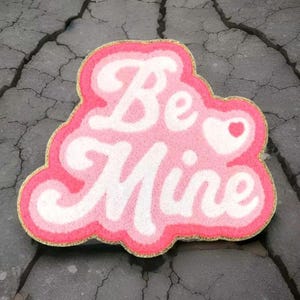 May include: Pink and white fuzzy doormat with the words "Be Mine" and a small heart.