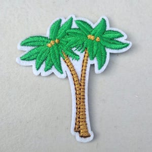 May include: Embroidered patch featuring two green palm trees with yellow accents and brown trunks. The patch has a white border. This tropical-themed patch is suitable for decorating clothing, bags, or other fabric items.