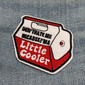 May include: Embroidered patch in the shape of a small cooler, with a white top and red base. The patch features the text "DON'T HATE ME BECAUSE I'M Little Cooler" in black and red lettering, outlined in black. The patch is on a denim background.