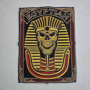 May include: Embroidered patch with a black background, featuring a gold skull wearing an Egyptian pharaoh headdress. The word "EGYPTIAN" is arched above the skull. Red and gold accents frame the design.