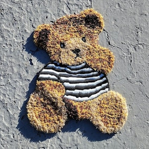 May include: A brown teddy bear with a black and white striped shirt. The bear is sitting on a gray surface.