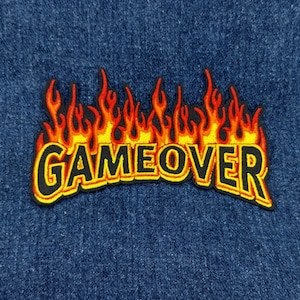May include: A black and yellow embroidered patch with the words "GAME OVER" in a bold font, set against a backdrop of stylized flames.