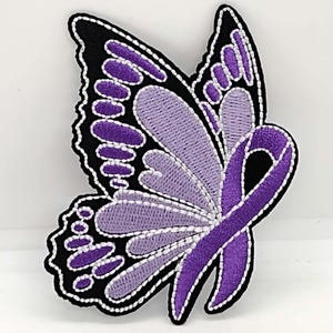 May include: Purple embroidered butterfly with a purple ribbon. The butterfly has black outlines and white stitching.