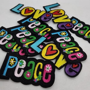 May include: A collection of colorful embroidered iron-on patches with the words "Love" and "Peace" in a variety of fonts and colors. The patches feature flowers, hearts, and other decorative elements.