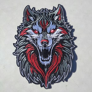 May include: Embroidered patch featuring a detailed wolf head with an open mouth, showcasing sharp teeth. The design incorporates red, blue, gray, and white thread on a black background, with a white border. The wolf's eyes are a striking red.
