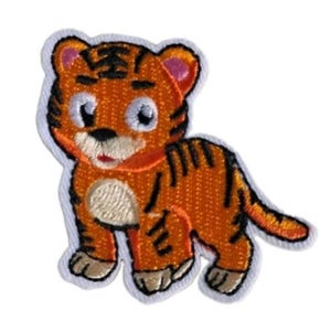 May include: An embroidered patch featuring a cartoon tiger cub with bright orange fur, black stripes, a white muzzle, and pink inner ears. The design has a white border outline and shows the tiger standing in a side profile with a small tail.