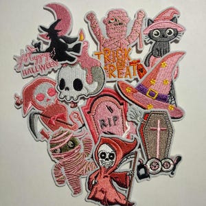 May include: A collection of embroidered Halloween patches in pink, black, and white. Designs include a witch on a crescent moon, a mummy, a black cat in a witch hat, a skull, a tombstone, and a grim reaper. Text includes "Happy Halloween" and "Trick or Treat".