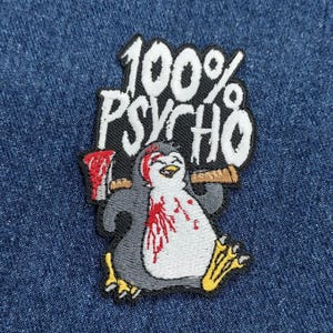 May include: An embroidered patch featuring a cartoon penguin holding a bloody axe. The penguin is wearing a white and gray outfit and has a red stain on its chest. The text "100% PSYCHO" is above the penguin.