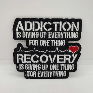 May include: Black embroidered patch with white text that reads "Addiction is giving up everything for one thing. Recovery is giving up one thing for everything." A red heart is included in the design.