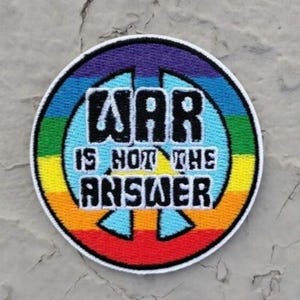 May include: A round, rainbow-colored patch with a peace sign in the center. The text "WAR IS NOT THE ANSWER" is written in black letters on the patch.