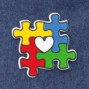 May include: A colorful puzzle piece design with a white heart in the center. The puzzle pieces are yellow, red, green, and blue.