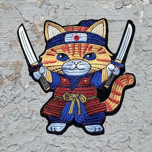 May include: A yellow and orange cat wearing a blue and red samurai outfit with two swords. The cat has a blue headband with a red circle in the middle.