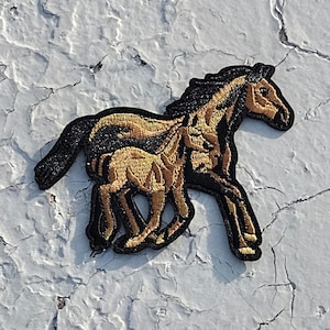 May include: A black and gold embroidered patch of a horse and foal running. The horse and foal are both facing right.