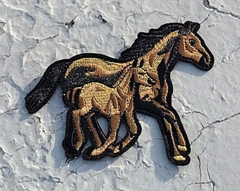 May include: A black and gold embroidered patch of a horse and foal running. The horse and foal are both facing right.