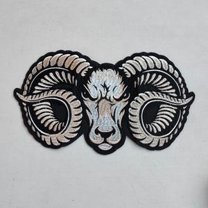 May include: A black embroidered patch with a silver ram's head and large curled horns.