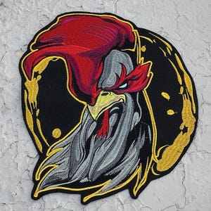 May include: Embroidered patch featuring a rooster with a red comb and wattle, a yellow beak, and a gray and white body. The rooster is surrounded by a gold horseshoe.