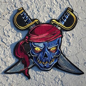 May include: A blue skull with yellow eyes wearing a red bandana and crossed swords. The skull is embroidered on a black fabric patch.