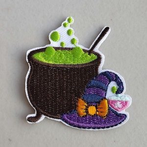 May include: Embroidered patch featuring a brown cauldron filled with green bubbling liquid and a spoon. A purple and blue witch hat with an orange bow is next to the cauldron. The patch has a white border and is likely for Halloween.