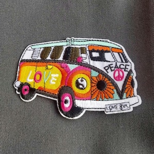 May include: An embroidered patch shaped like a van with a white, yellow, and orange color scheme. The side features the word LOVE in white letters, while the front displays the word PEACE with a symbol and the text LOVE BUS on the bumper.