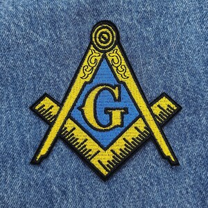 May include: A yellow and blue embroidered patch depicting a compass and square, a common symbol of Freemasonry. The letter "G" is centered within the square.