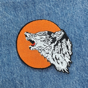 May include: A white wolf howling at the moon, embroidered on a patch with an orange background.