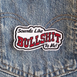 May include: Embroidered patch with the phrase "Sounds Like BULLSHIT To Me!" in red and black lettering on a white background. The patch is bordered in black and white and is affixed to a denim pocket.