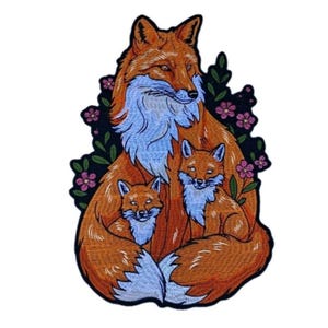 May include: Embroidered patch featuring a family of foxes. The mother fox is orange with a light blue chest and is surrounded by two smaller foxes. Dark green leaves and pink flowers frame the foxes.