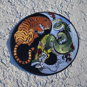 May include: A black and white yin yang symbol with a tiger on one side and a dragon on the other. The tiger is orange and black, and the dragon is green and blue.