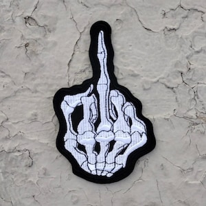 May include: White embroidered skeleton hand giving the middle finger on a black patch.