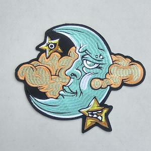 May include: A crescent moon with a face, a cloud, and two stars. The moon is turquoise, the cloud is orange, and the stars are gold. The patch is embroidered and has a black border.