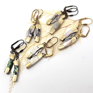 May include: A set of four pairs of earrings featuring miniature pocket knives with different colored mother-of-pearl inlays. The earrings are made of gold-toned metal and have a hook closure.