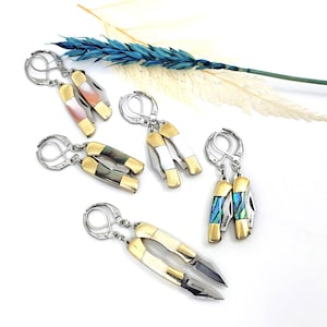 Puede incluir: Conjunto de cinco pares de pendientes con navajas de bolsillo en miniatura con mangos de diferentes colores. Las navajas están hechas de metal dorado y plateado y tienen un diseño detallado. Los pendientes son perfectos para añadir un toque único y atrevido a cualquier atuendo.