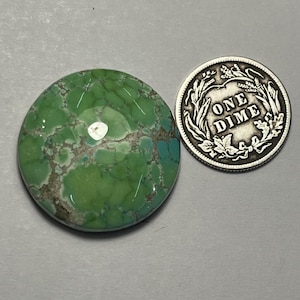 May include: A round, green turquoise cabochon with a marbled pattern. The cabochon is approximately the size of a US dime.