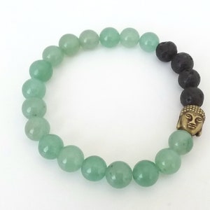 Puede incluir: Un brazalete de cuentas verdes y negras con un dije de Buda dorado. El brazalete está hecho con cuentas de jade verde y roca de lava negra.