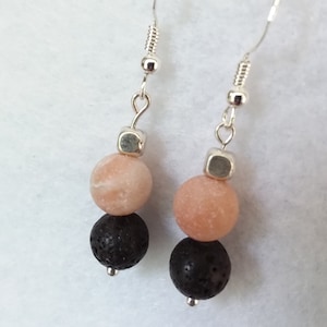 Może przedstawiać: Para srebrnych kolczyków z dwoma koralikami na każdym. Górny koralik jest jasnoróżowy, a dolny czarny.