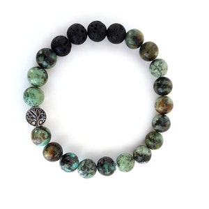 May include: A bracelet made with black lava rock and green turquoise beads. A silver charm with a tree design is included.