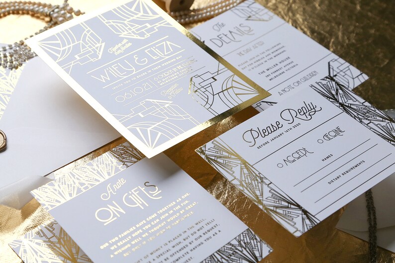 May include: A set of wedding stationery with a gold and pale grey Art Deco theme. The suite includes an invitation, details card, reply card, and gift information card. The invitation features the names "Wiley & Eliza" and the date "06.10.21".