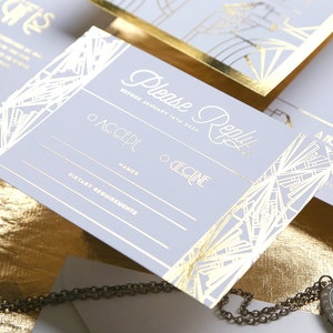 May include: Art Deco style wedding invitation set. The invitation and response card feature gold foil detailing on a pale grey background. The invitation includes the words "Please Reply" and RSVP information.