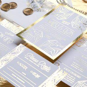 May include: A set of wedding invitations with gold foil detailing. The suite includes invitation cards, RSVP, details, and gift information cards. The design features art deco style geometric patterns and gold foil edging. The invitations are on a light grey background.