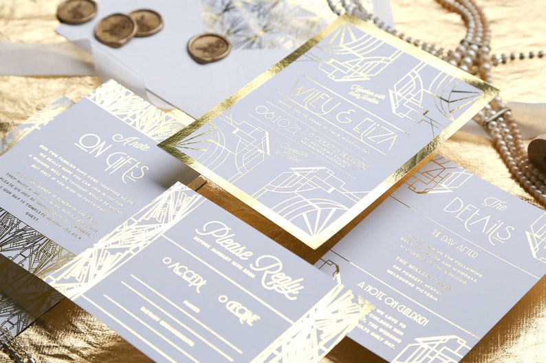 May include: A set of wedding invitations with gold foil detailing. The suite includes invitation cards, RSVP, details, and gift information cards. The design features art deco style geometric patterns and gold foil edging. The invitations are on a light grey background.