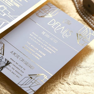 May include: Light grey wedding stationery with gold foil art deco detailing. The invitation text is in gold, including the date, time, and venue. The stationery is displayed on a gold textured surface.