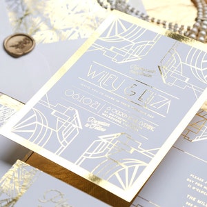 May include: A stylish wedding invitation set with gold foil accents on a pale grey background. The invitation displays the names "Wiley & Eliza" and event details. Includes matching envelopes and wax seals.