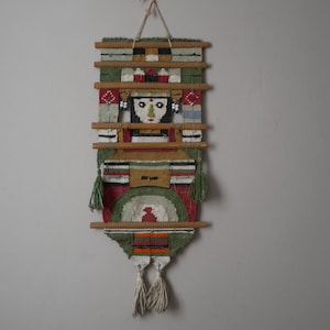 Peut inclure: Une tapisserie murale tissée avec un motif géométrique coloré mettant en scène un visage humain stylisé au centre. La tapisserie est faite de fils de différentes couleurs et possède un cadre en bois.