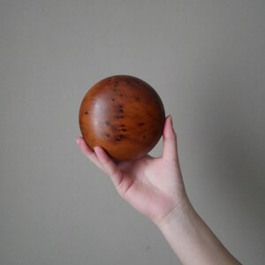 Op de afbeelding: Een gladde, ronde houten bal met een donkerbruine kleur en een natuurlijk houtnerfpatroon.