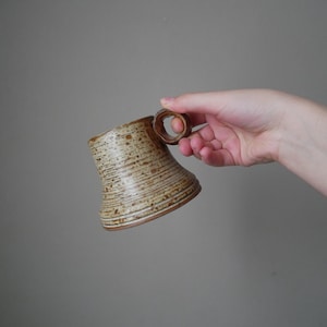 May include: A brown and beige ceramic mug with a ring handle. The mug has a textured, striped design.