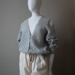 Op de afbeelding: Een lichtblauwe gebreide cardigan met een ruitpatroon en een v-hals. De cardigan heeft een knoopsluiting en lange mouwen.