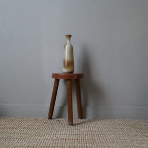 Peut inclure: Un vase en céramique brun et blanc posé sur un tabouret en bois brun avec un dessus en cuir. Le tabouret a trois pieds et se trouve sur un tapis tissé.