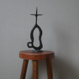 Può includere: Un candelabro in metallo nero con un design unico e astratto. Il candelabro è posto su uno sgabello in legno marrone con un piano in pelle.
